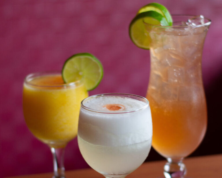 Three festive cocktails in a restaurant setting on a wooden table and a pink background