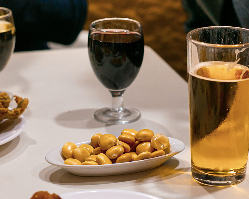 tall glass of beer, a glass of wine and small plate of lupin beans on a white table