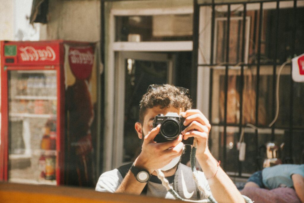 A young man capturing his reflection in an urban setting with a camera.